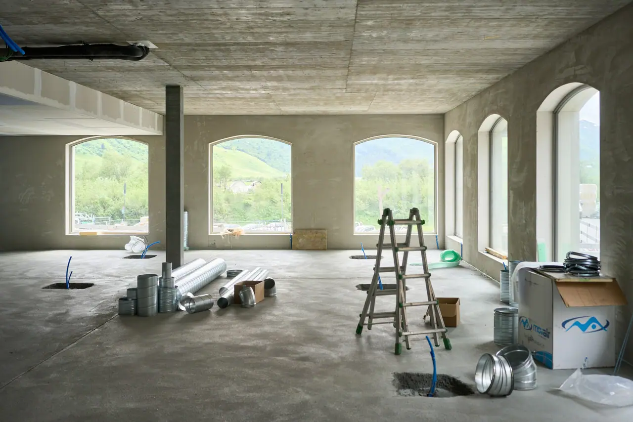 Un plateau en travaux : gaines posées au sol, escabeau, grandes fenêtres cintrées.