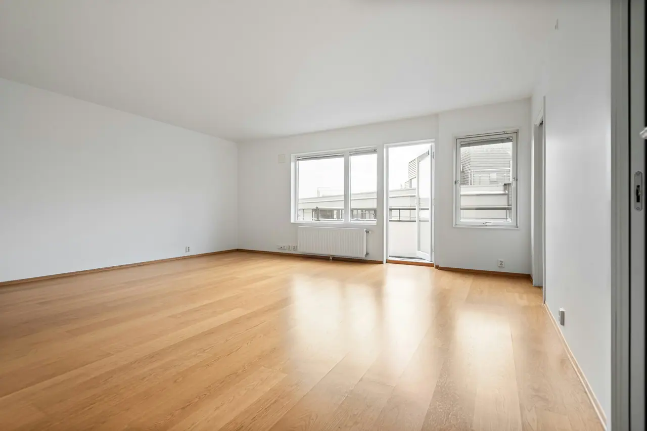 Séjour vide d’un logement, parquet clair et grandes fenêtres.